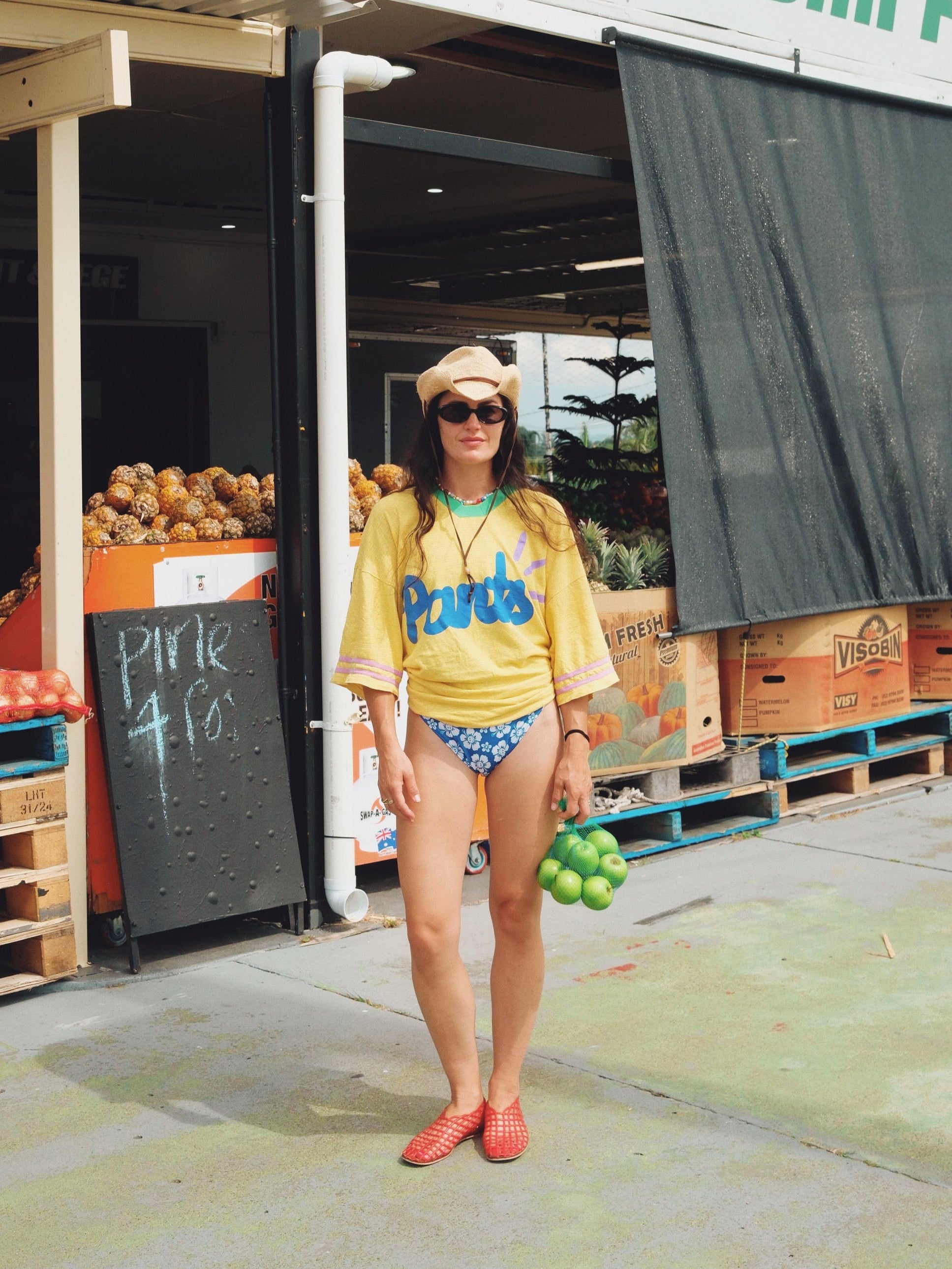 Person in a yellow shirt and blue shorts standing in front of Nundah Fruits store