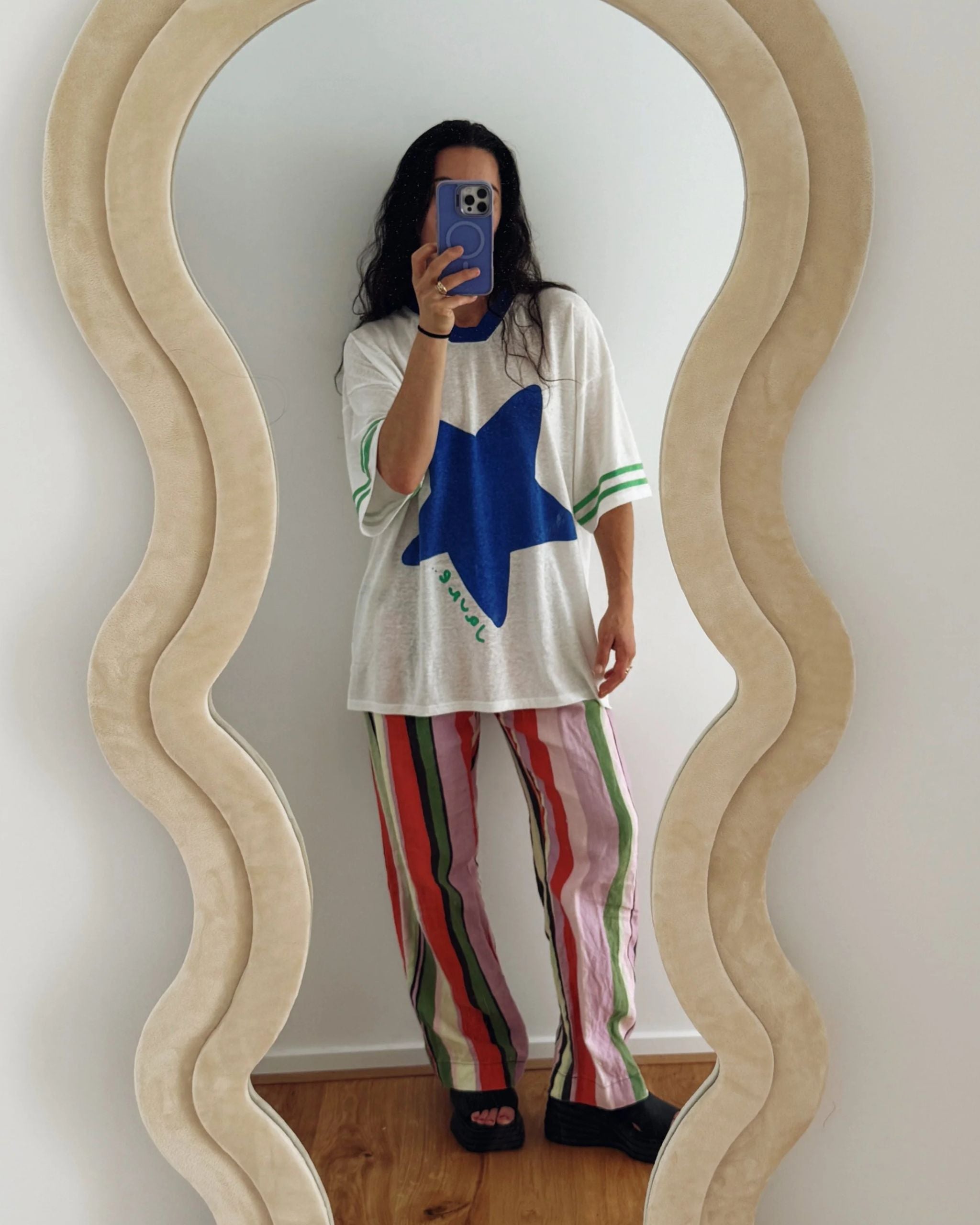 Woman showing her outfit in a mirror wearing a white hemp and tencel adult tee with a blue star and green textured sleeve stripes by Yolky Club