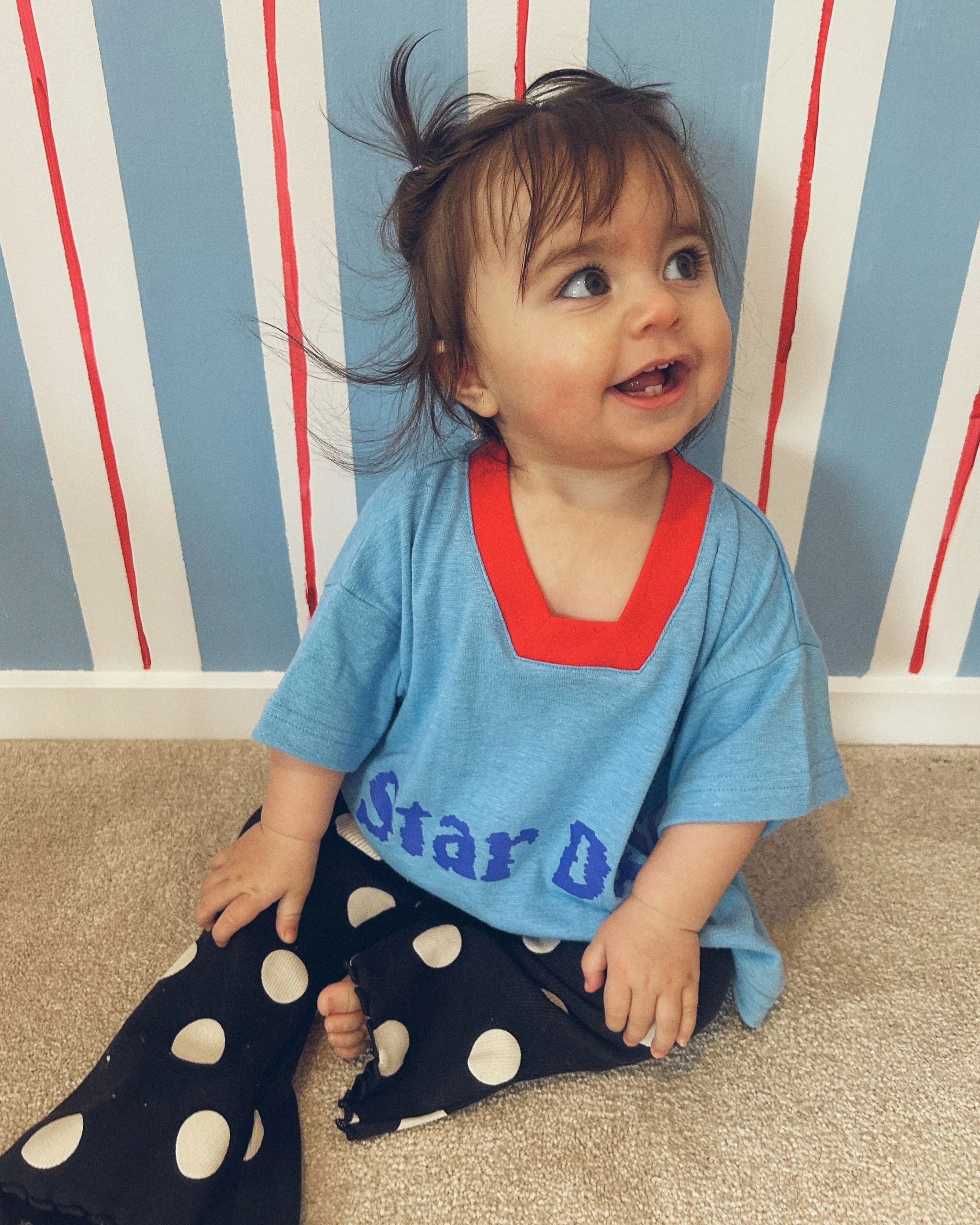 Toddler wearing a blue hemp, recycled polyester and tencel kids t-shirt with a red neckline trim with text reading Star Dust, by Yolky Club.