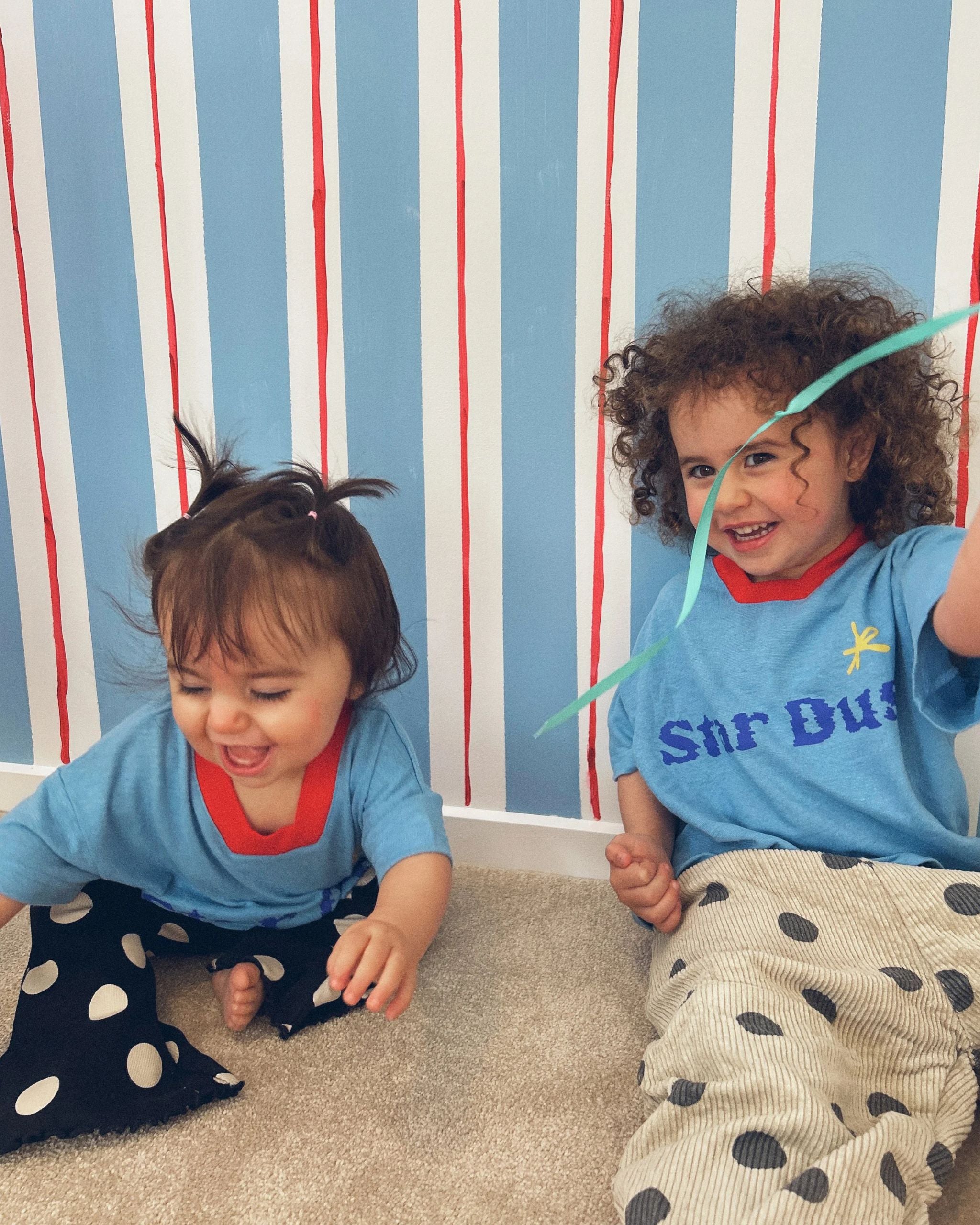 Two children wearing a blue hemp, recycled polyester and tencel kids t-shirt with text reading Star Dust, by Yolky Club.