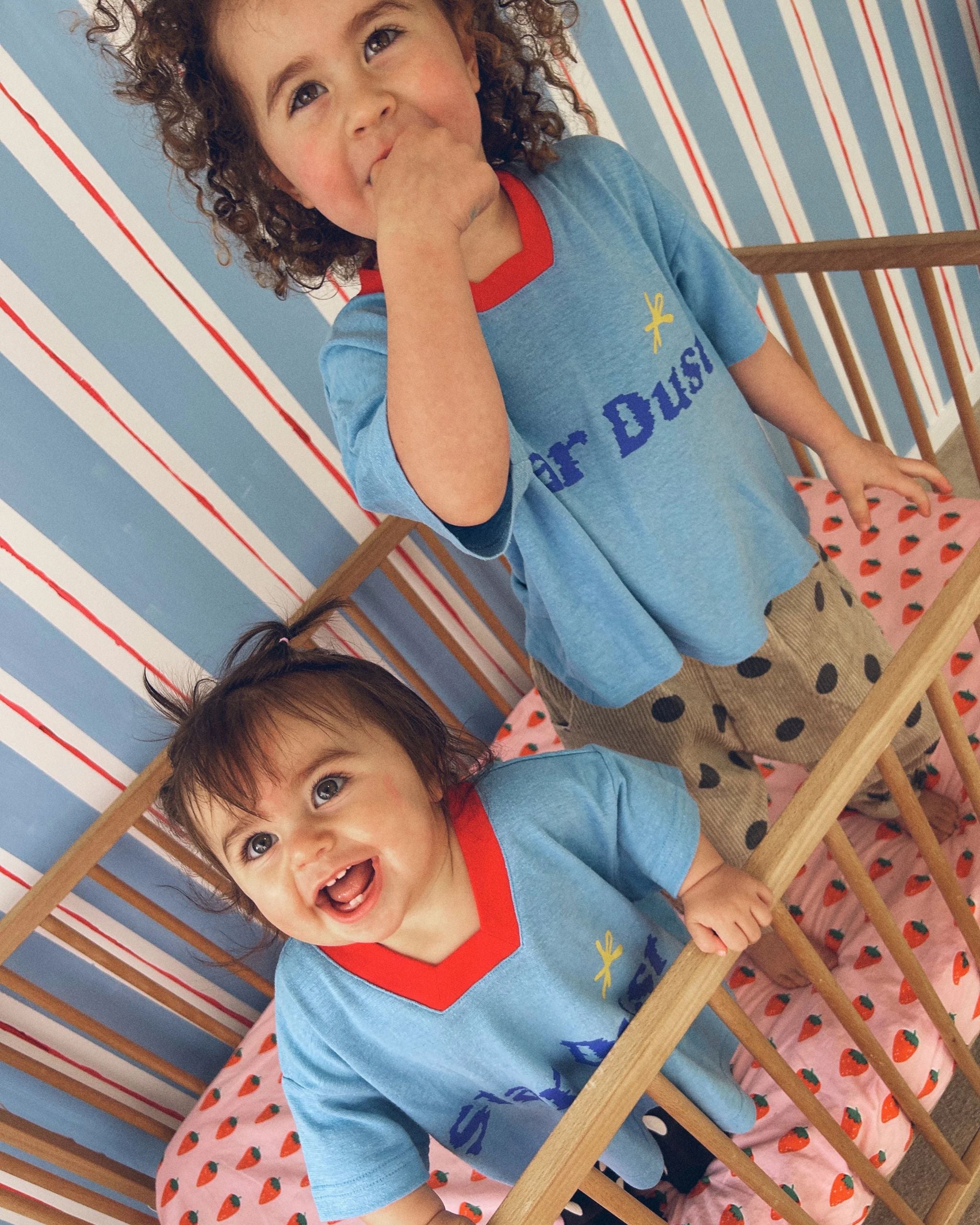 Two children wearing a blue hemp, recycled polyester and tencel kids t-shirt with text reading Star Dust, by Yolky Club.