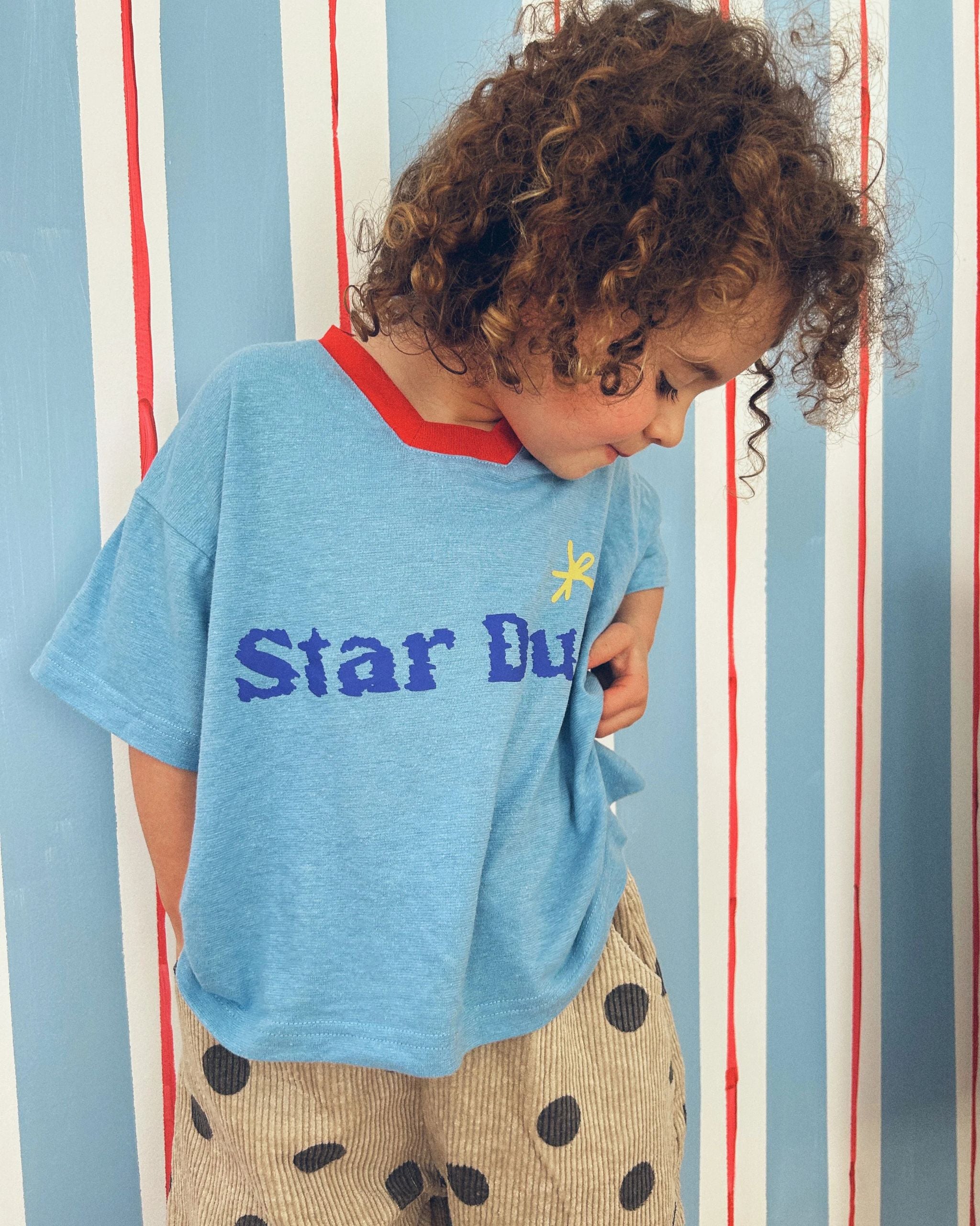 Child wearing a blue hemp, recycled polyester and tencel kids t-shirt with text reading Star Dust, by Yolky Club.
