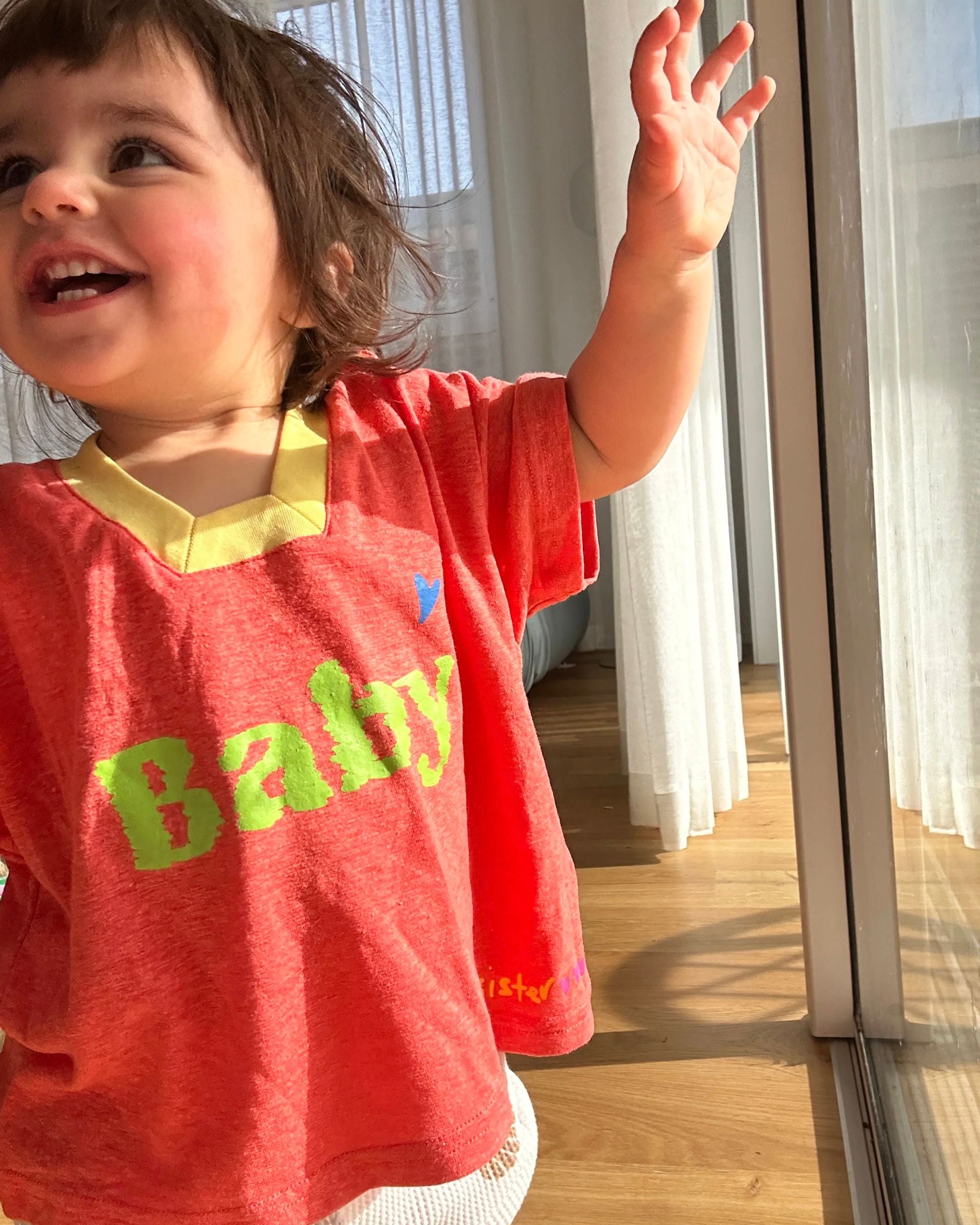 Orange-peach hemp and tencel kids t-shirt with ‘baby sister’ print, worn by a child