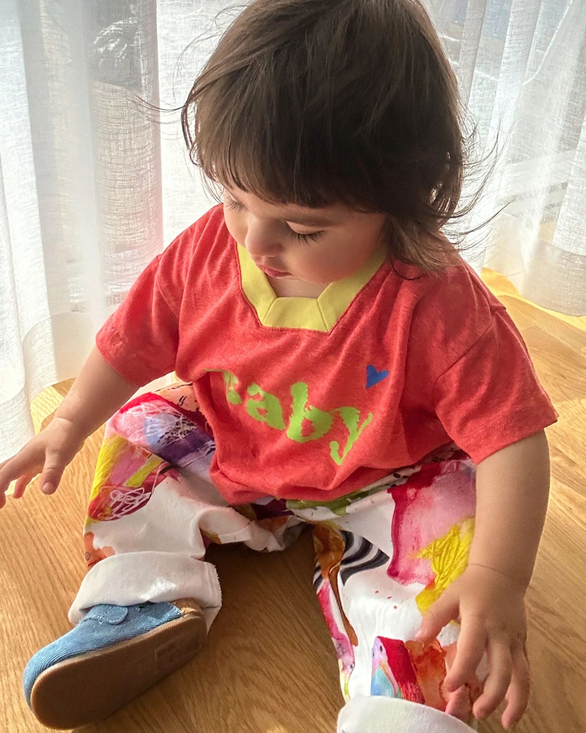 Child wearing an orange-peach hemp and tencel kids t-shirt with ‘baby sister’ text by Yolky Club