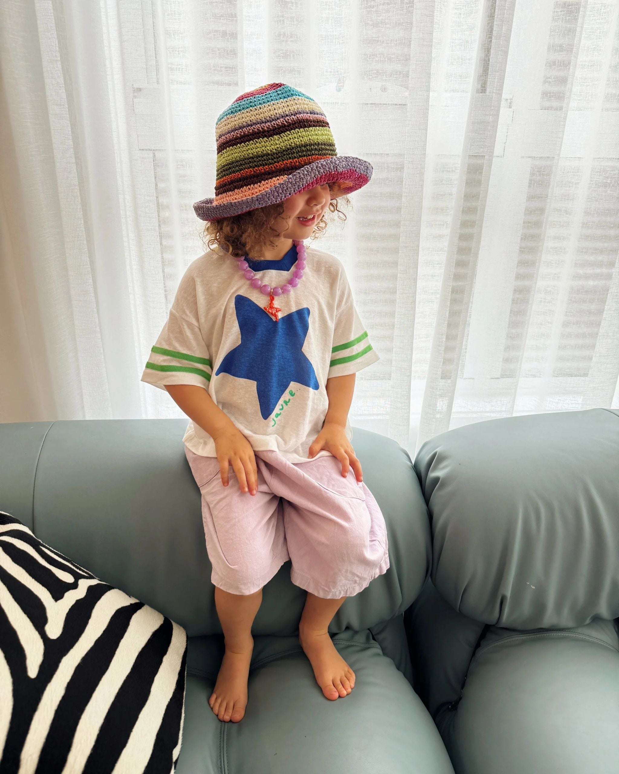 White hemp and tencel kids t-shirt with blue star print and green sleeve stripes, worn by a child on a couch