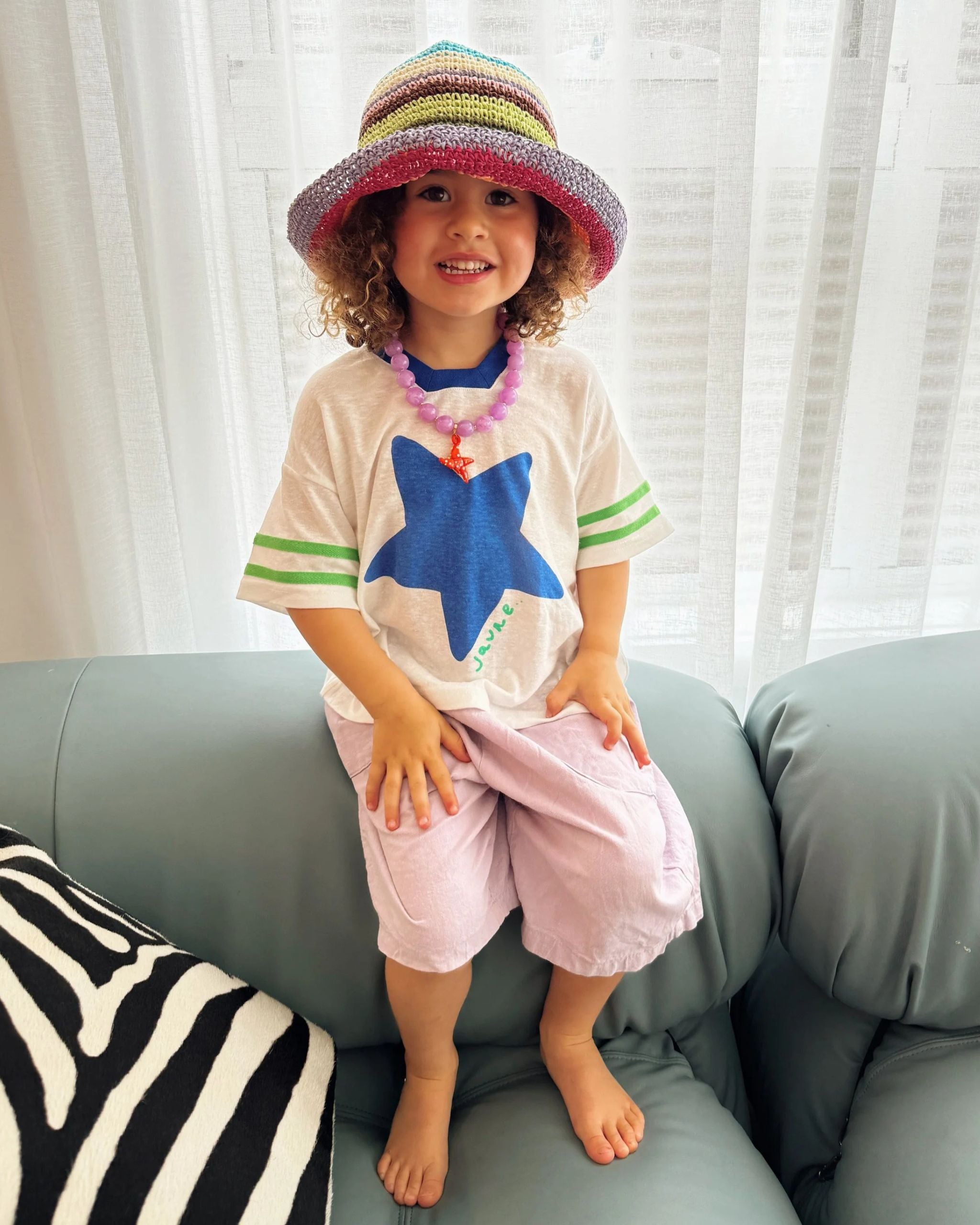 Child showing a colorful outfit while wearing a white hemp and tencel kids tee with blue star and green textured sleeve stripes by Yolky Club