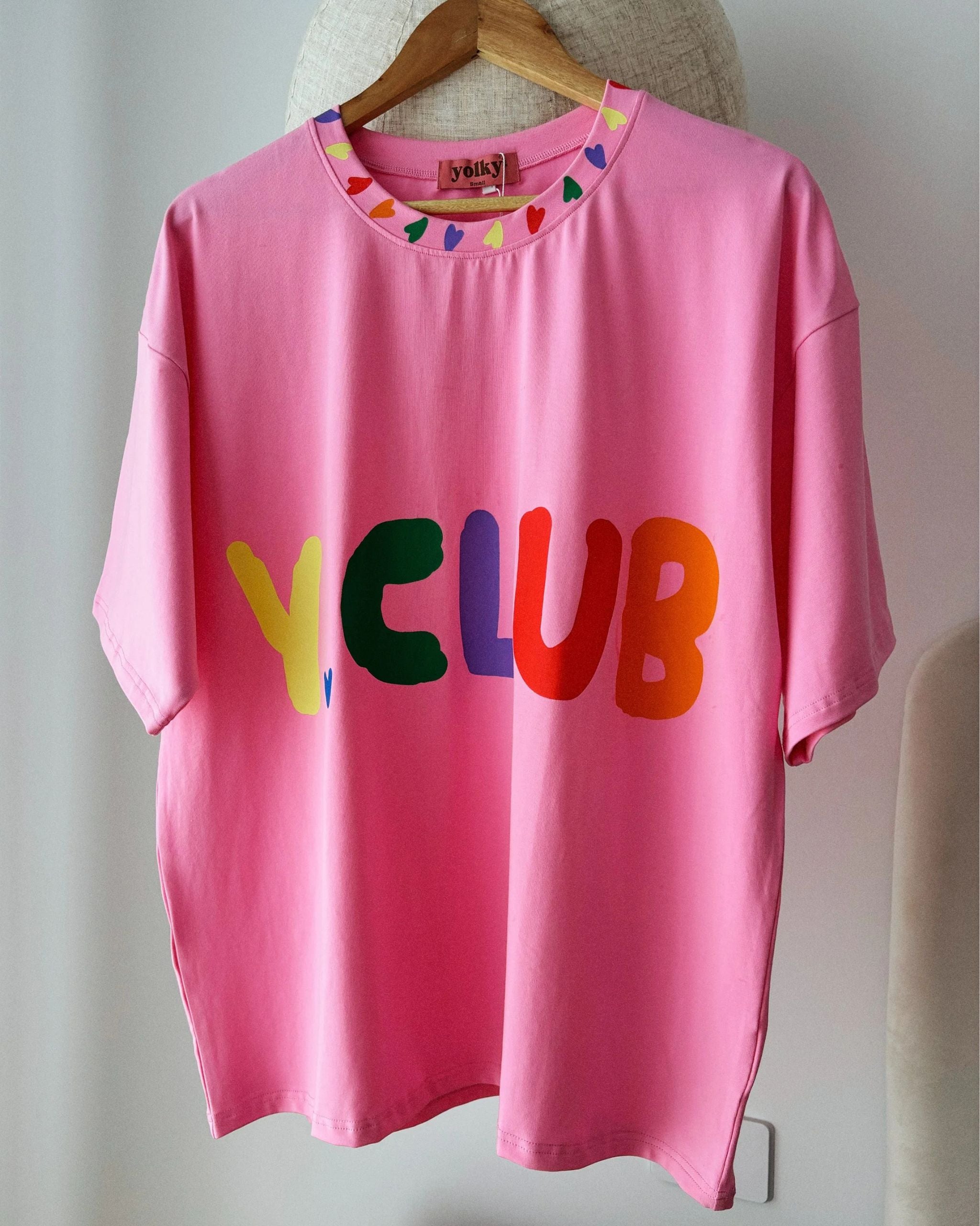 Close-up of pink organic cotton adult t-shirt with rainbow Y.CLUB text and heart illustrations by Yolky Club