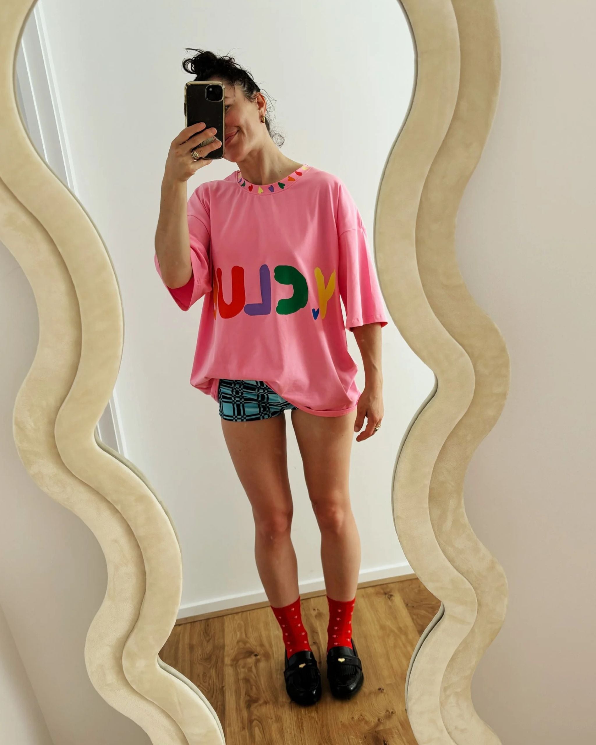 Woman wearing a pink organic cotton adult t-shirt with rainbow Y.CLUB text and small heart details by Yolky Club