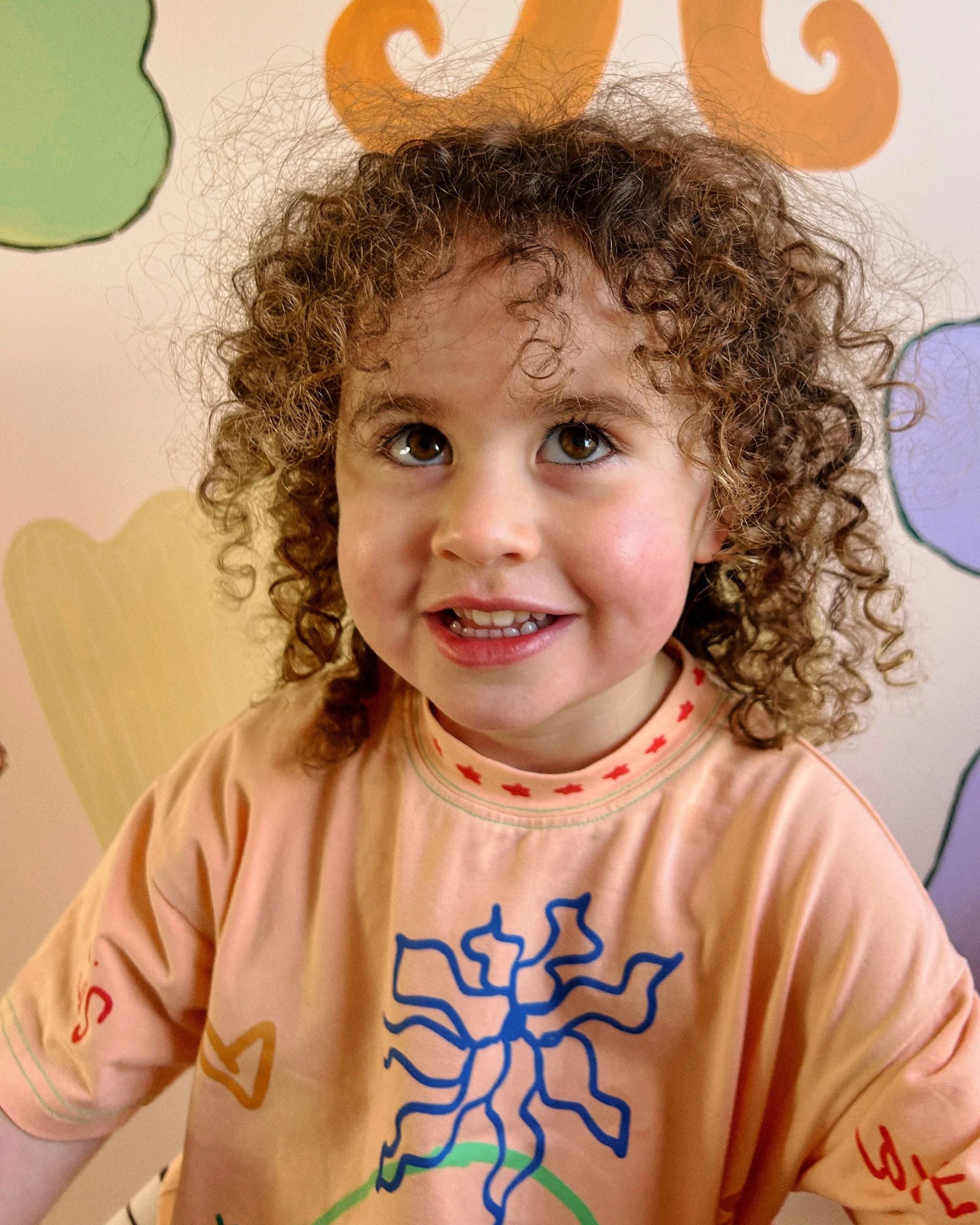 Close-up of child wearing an orange organic cotton kids t-shirt with hand-drawn illustrations by Yolky Club