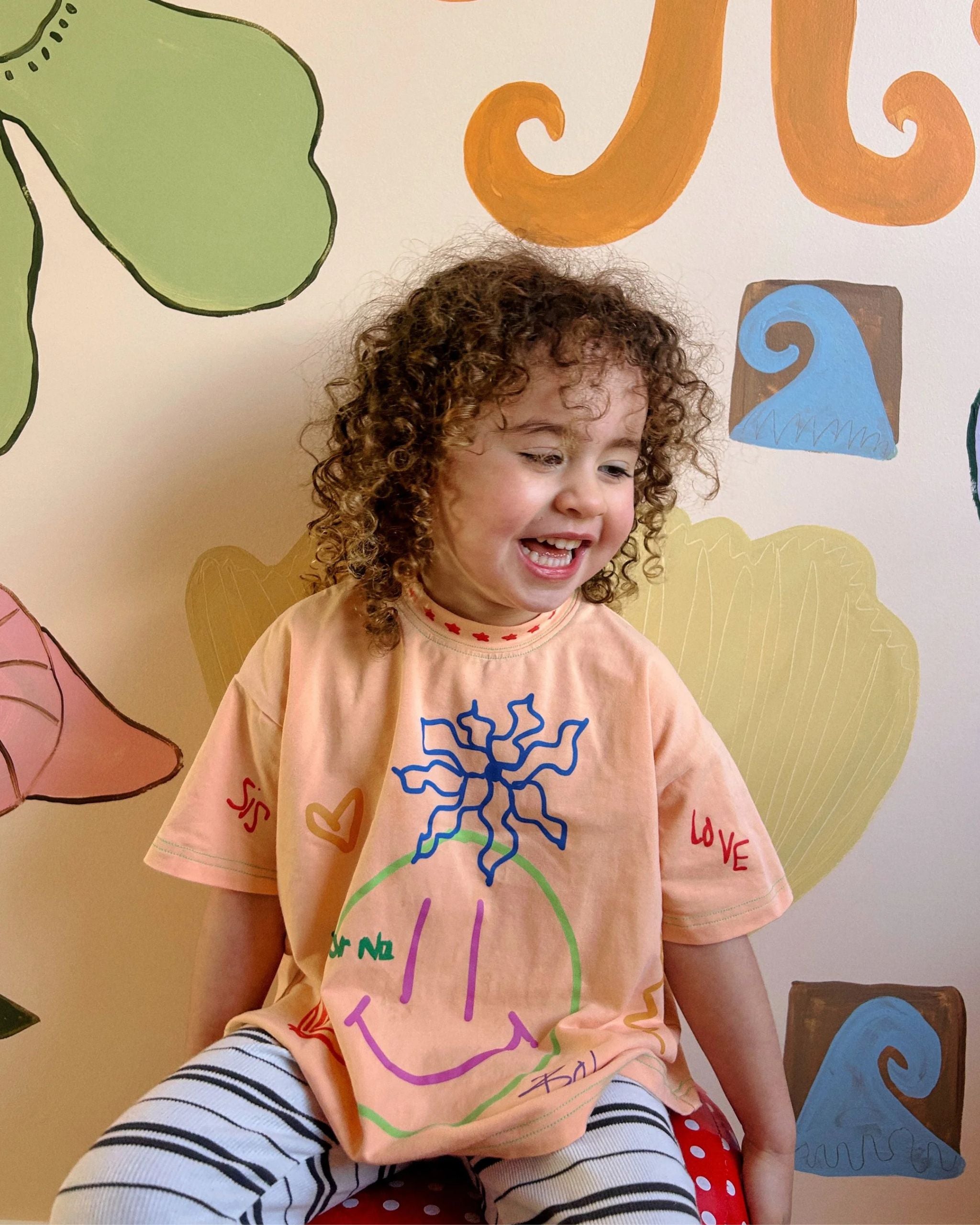 Orange organic cotton kids t-shirt with playful hand-drawn illustrations, worn by a child indoors