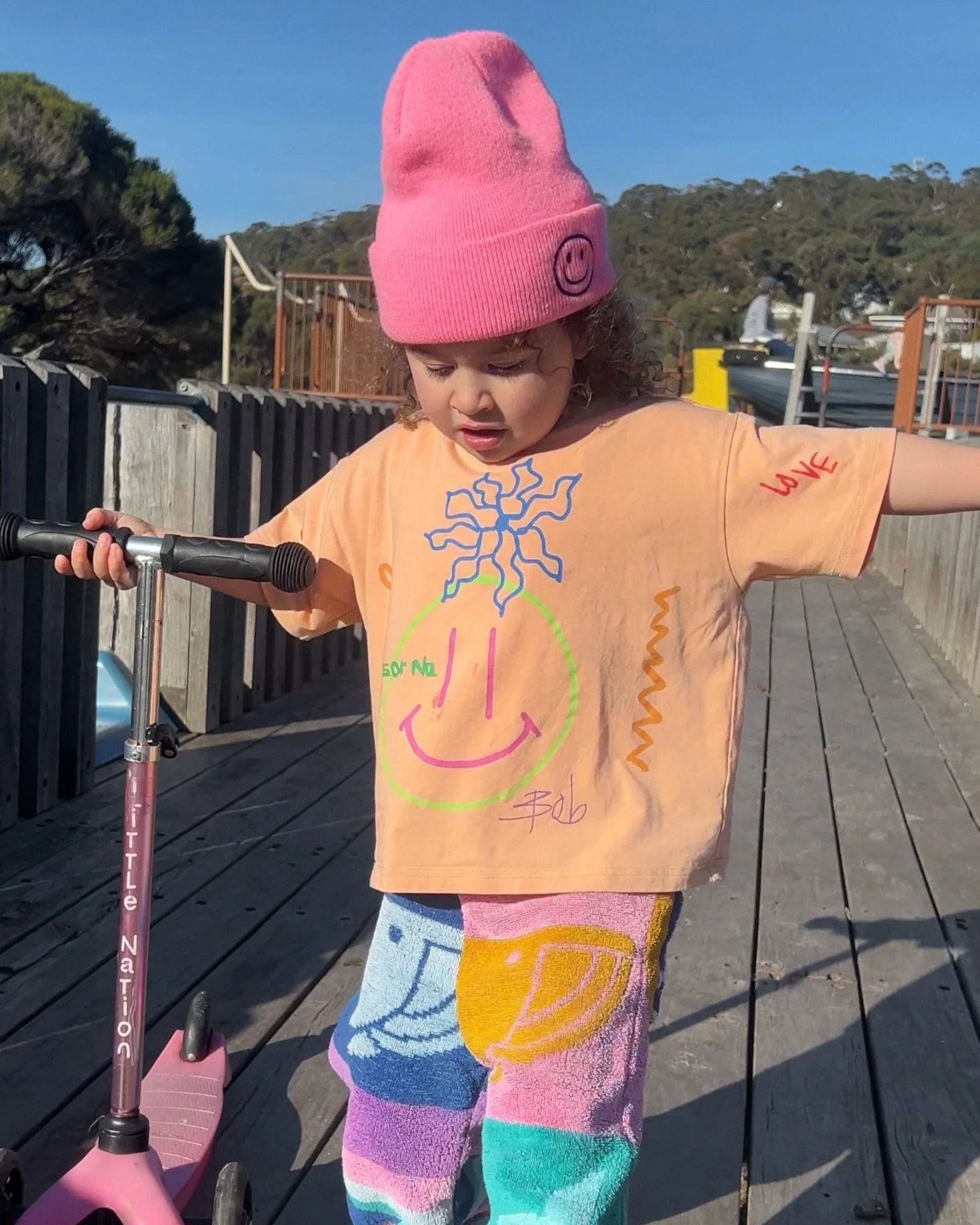Child wearing an orange organic cotton kids tee with hand-drawn illustrated designs by Yolky Club, playing outside