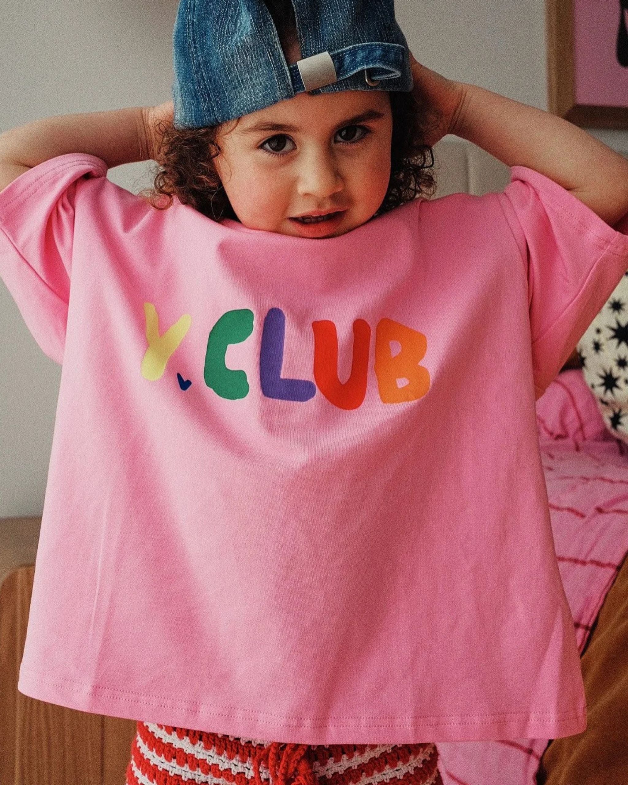 Young girl wearing a pink organic cotton kids t-shirt with rainbow Y.CLUB text and small heart details by Yolky Club